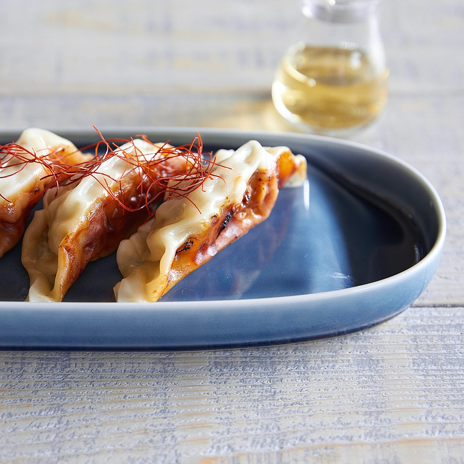 Three gyozas on a blue plate with a glass of white wine in the background.