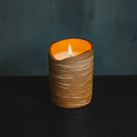 Candle in a textured brown container with a dark background
