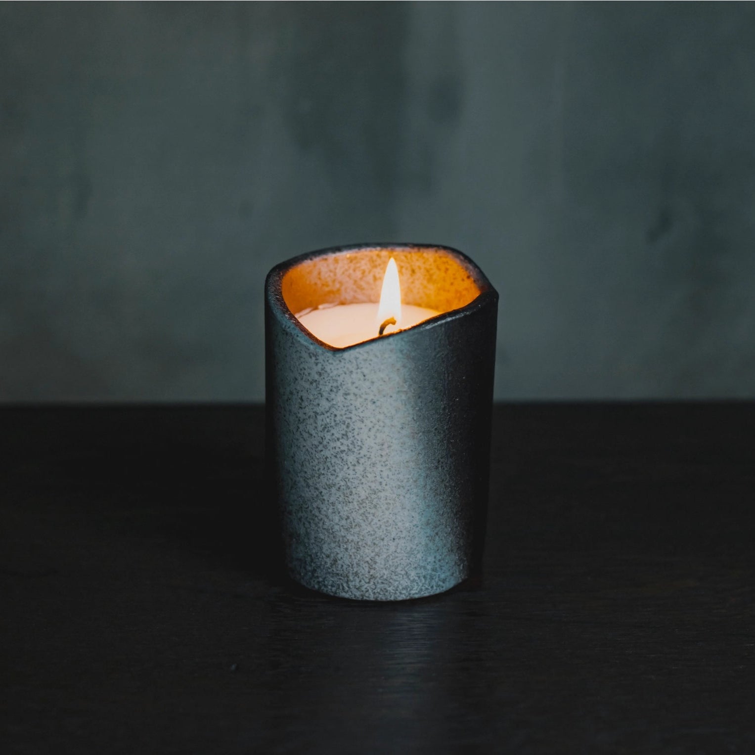 Candle in a textured holder on a dark surface with a dark background