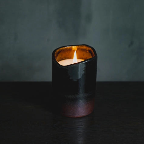 Black ceramic candle holder with a lit candle on a dark surface and background