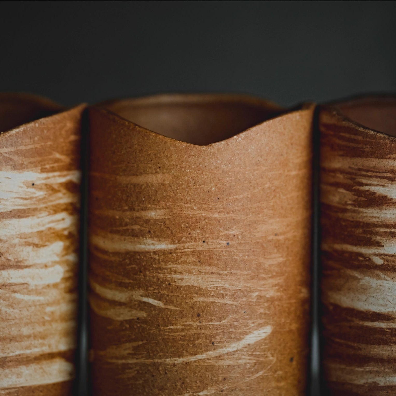 Three wooden candle holderrs with a textured surface on a dark background
