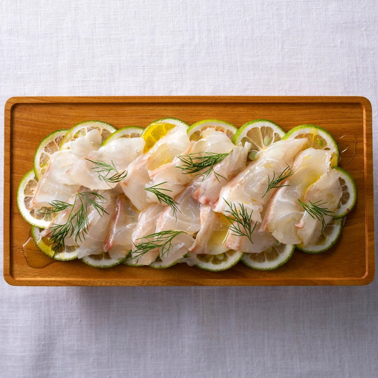 Raw fish fillets with lemon slices and herbs on a wooden platter.