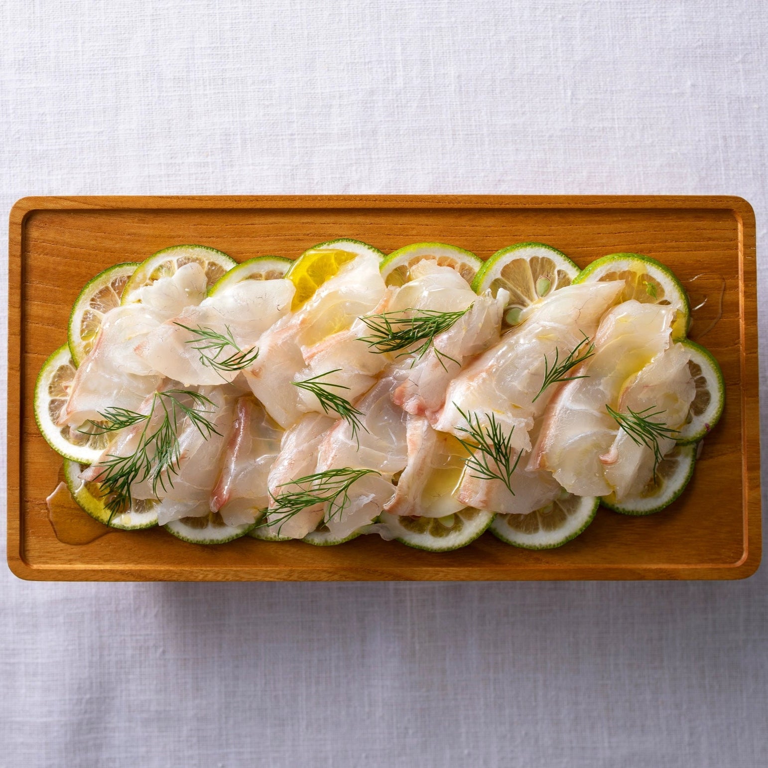 Raw fish fillets with lemon slices and herbs on a wooden platter.