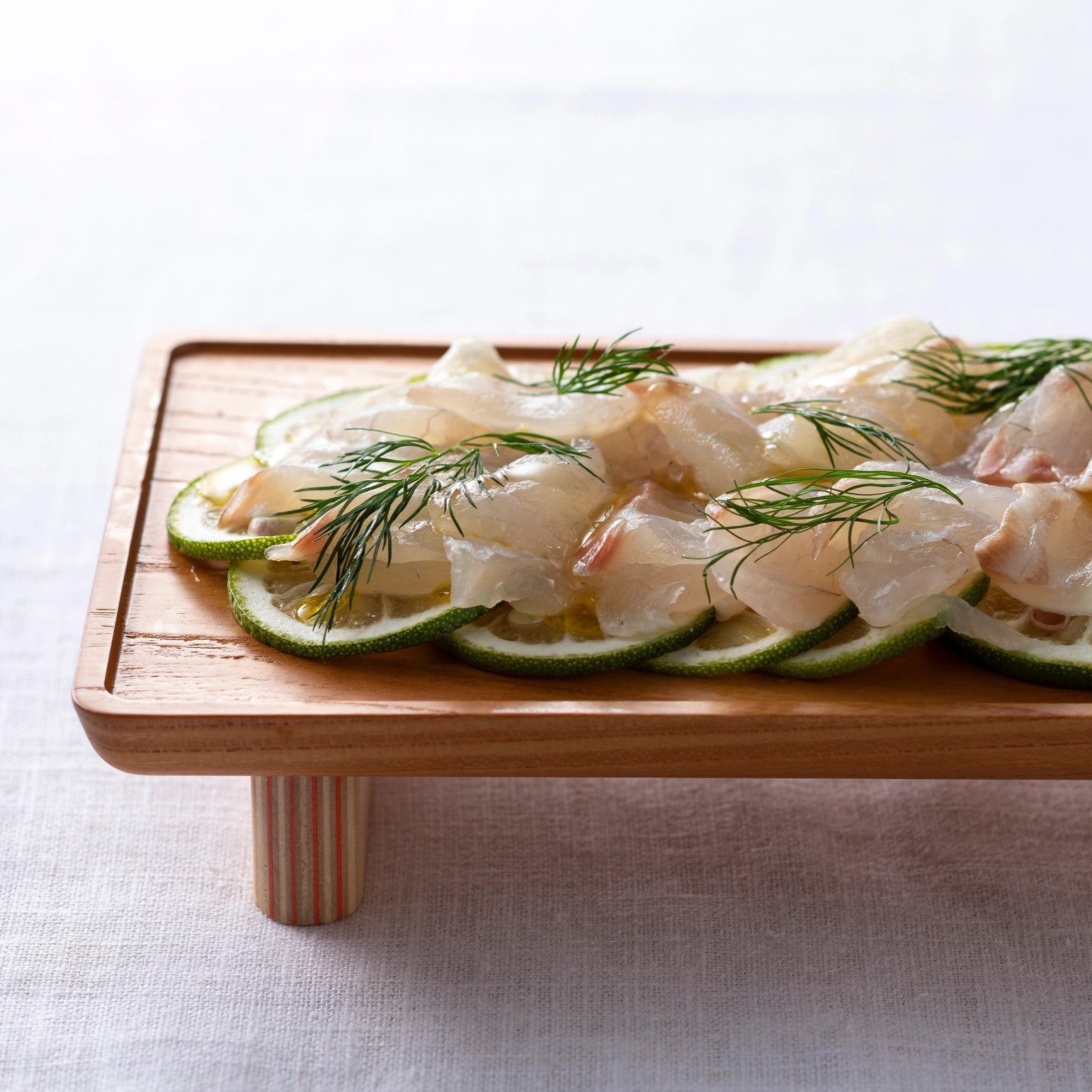 Raw fish fillets with lime slices and herbs on a wooden board