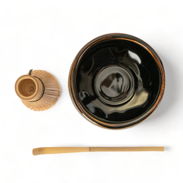 Black ceramic bowl with wooden whisk and spoon on a white background