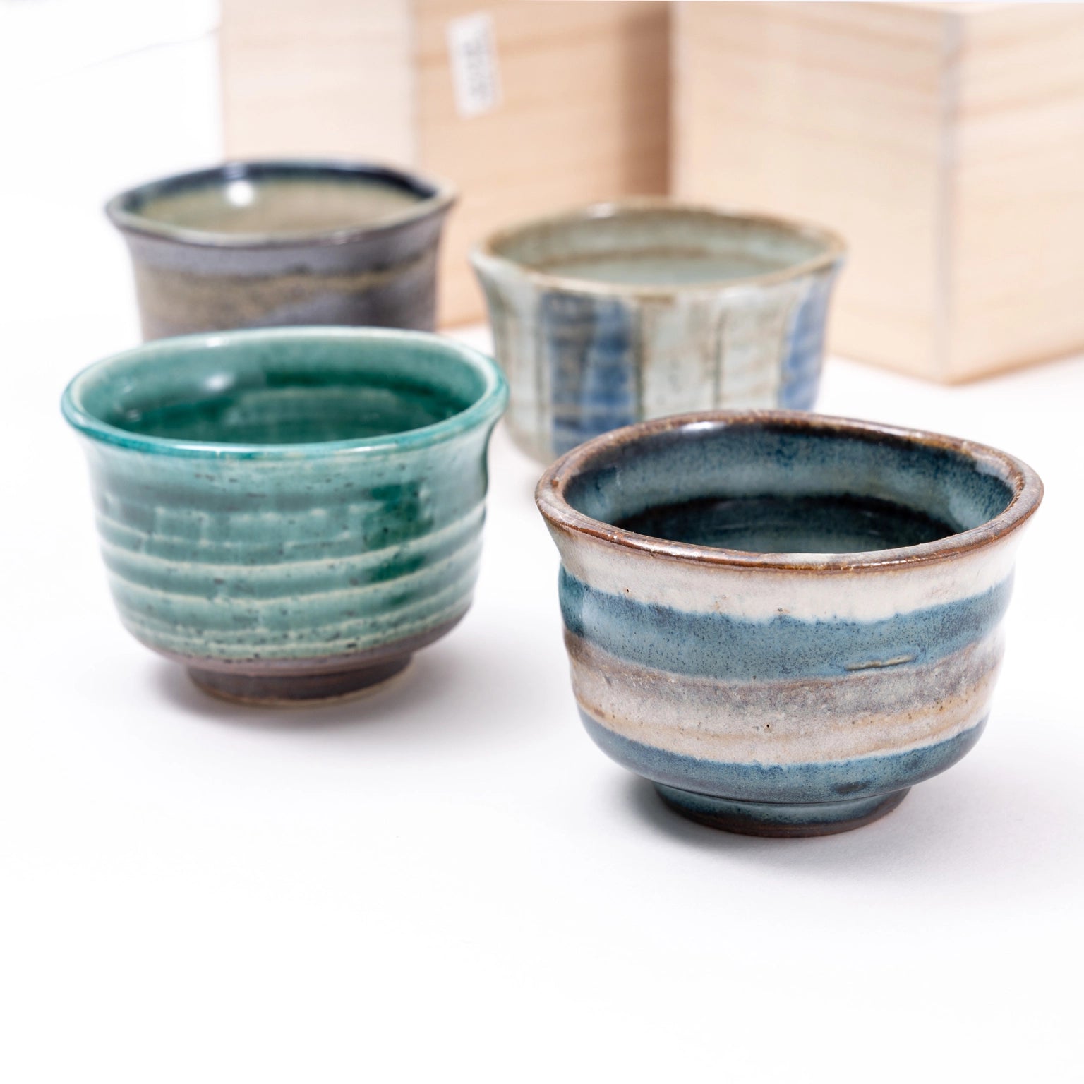 Four ceramic cups with blue and green glazes on a white surface.