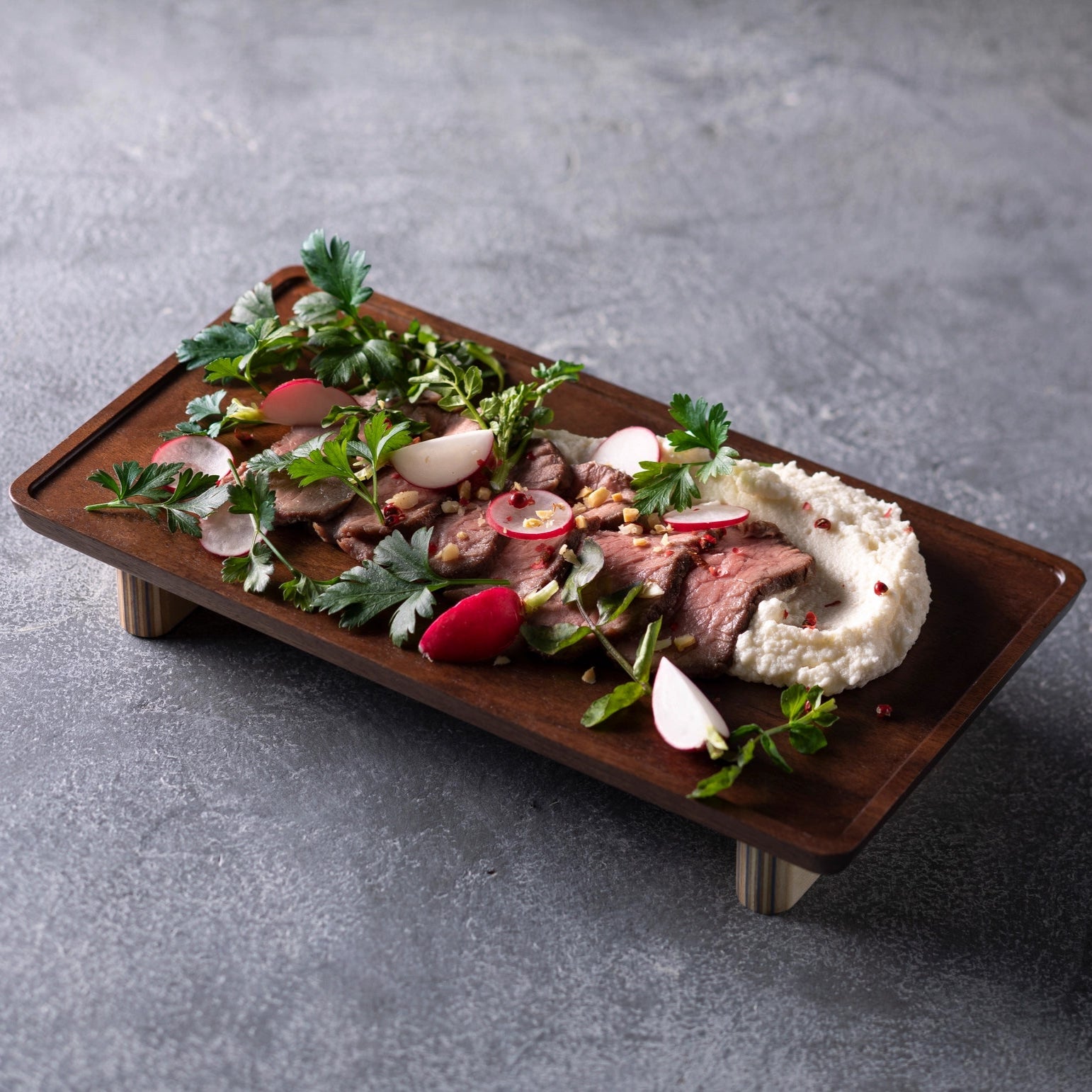 Plated dish with meat, vegetables, and a side of mashed potatoes on a gray surface