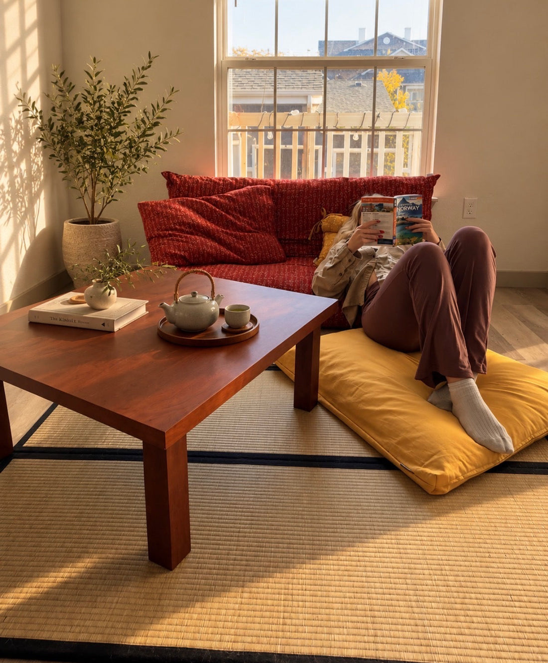 woman reading in a japanese inspired room with floor table, tatami mat, zabuton, shikifuton, incense, tea and plants