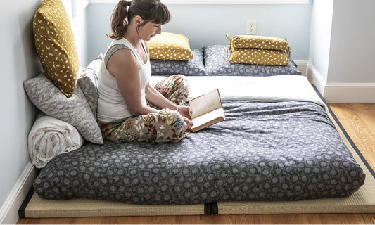 Woman sitting on shikifuton on top of tatami mat reading a book with supportive buckwheat hull and silk pillows