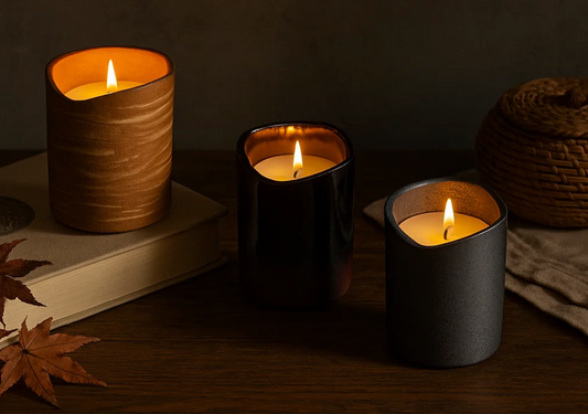 three candles sitting on a wooden table and book, lit with warm lighting and fall leaves