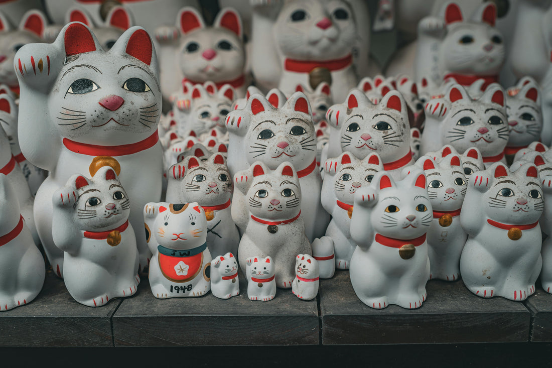 Many white Maneki Neko lucky cats placed next to one another on a cement shelf.