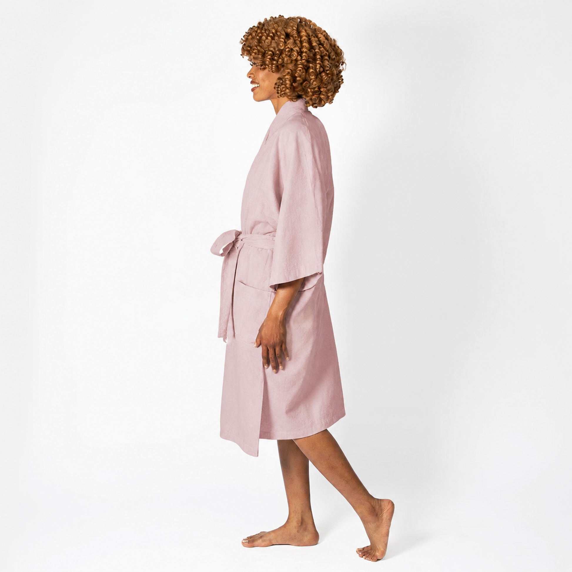 A woman wearing a light pink cotton robe, shown in profile against a plain white studio background.