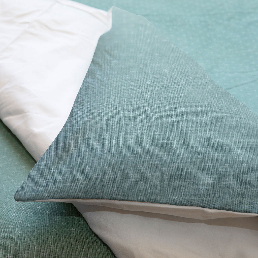 Close-up of textured teal fabric with a white pillow on a light blue background