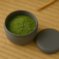 Dark gray container with green matcha powder on a wooden surface