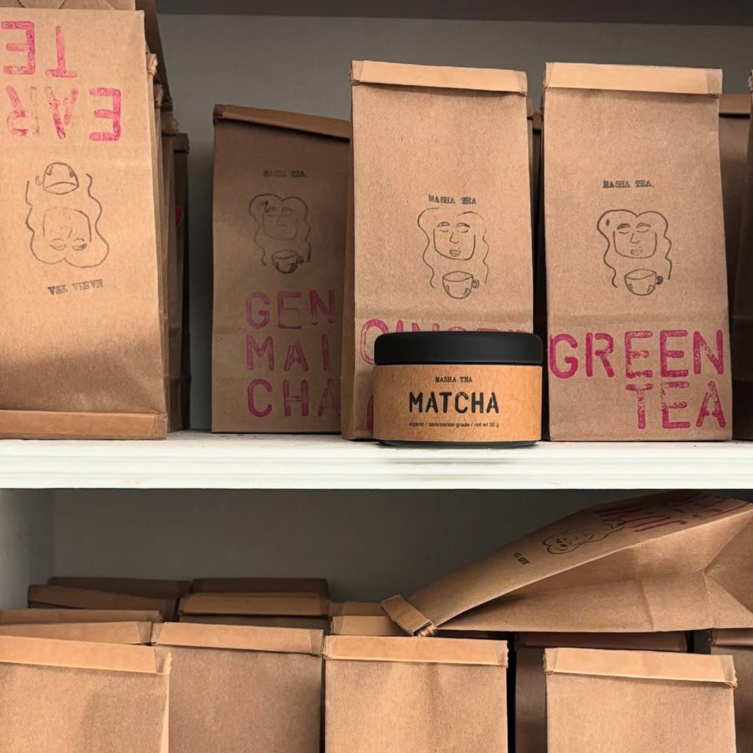 Brown bags of green tea on a shelf and a can of matcha powder.