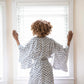 Woman standing at a window, looking outside while wearing a kimono-style Japanese robe. 