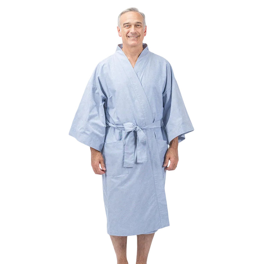 A smiling older man wearing a light blue kimono-style bathrobe with a tie belt, standing barefoot against a plain white studio background.