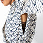 Close-up of a person wearing a white and navy blue patterned top with a wave or scallop motif, shown against a plain light background.