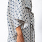 A close-up of a person wearing a loose, short-sleeved kaftan-style top with a navy blue and off-white scallop pattern, tied at the waist.