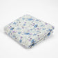 A folded blanket with a delicate blue and purple floral pattern on a white background, photographed on a seamless white studio background.