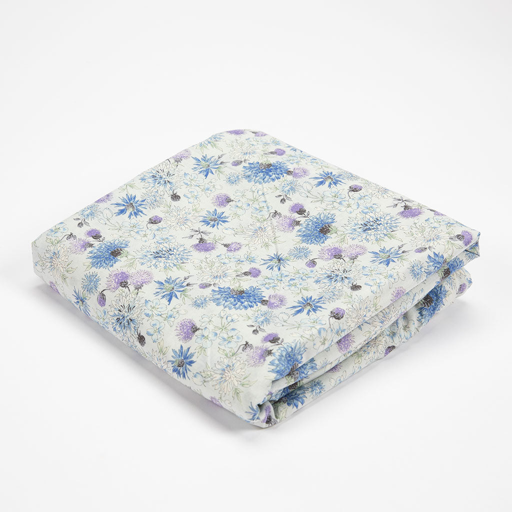 A folded blanket with a delicate blue and purple floral pattern on a white background, photographed on a seamless white studio background.