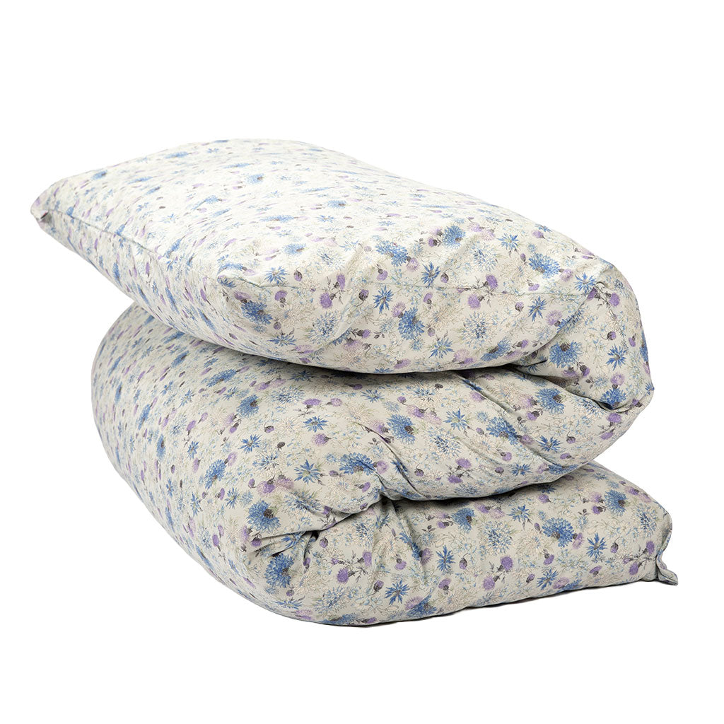 A shiki futon mattress folded with a small blue and purple floral pattern on a light beige background, isolated on a white background.