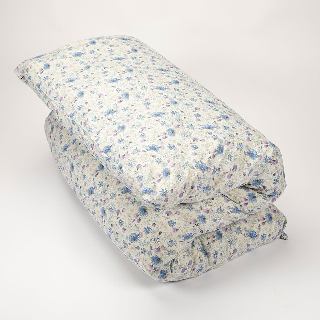 A shikifuton mattress folded. The fabric features a dense small floral print in blue and purple on a warm off-white base.