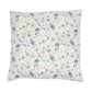 A square decorative throw pillow featuring a delicate floral print with blue and purple flowers on a warm cream background, shown against a plain white studio backdrop.