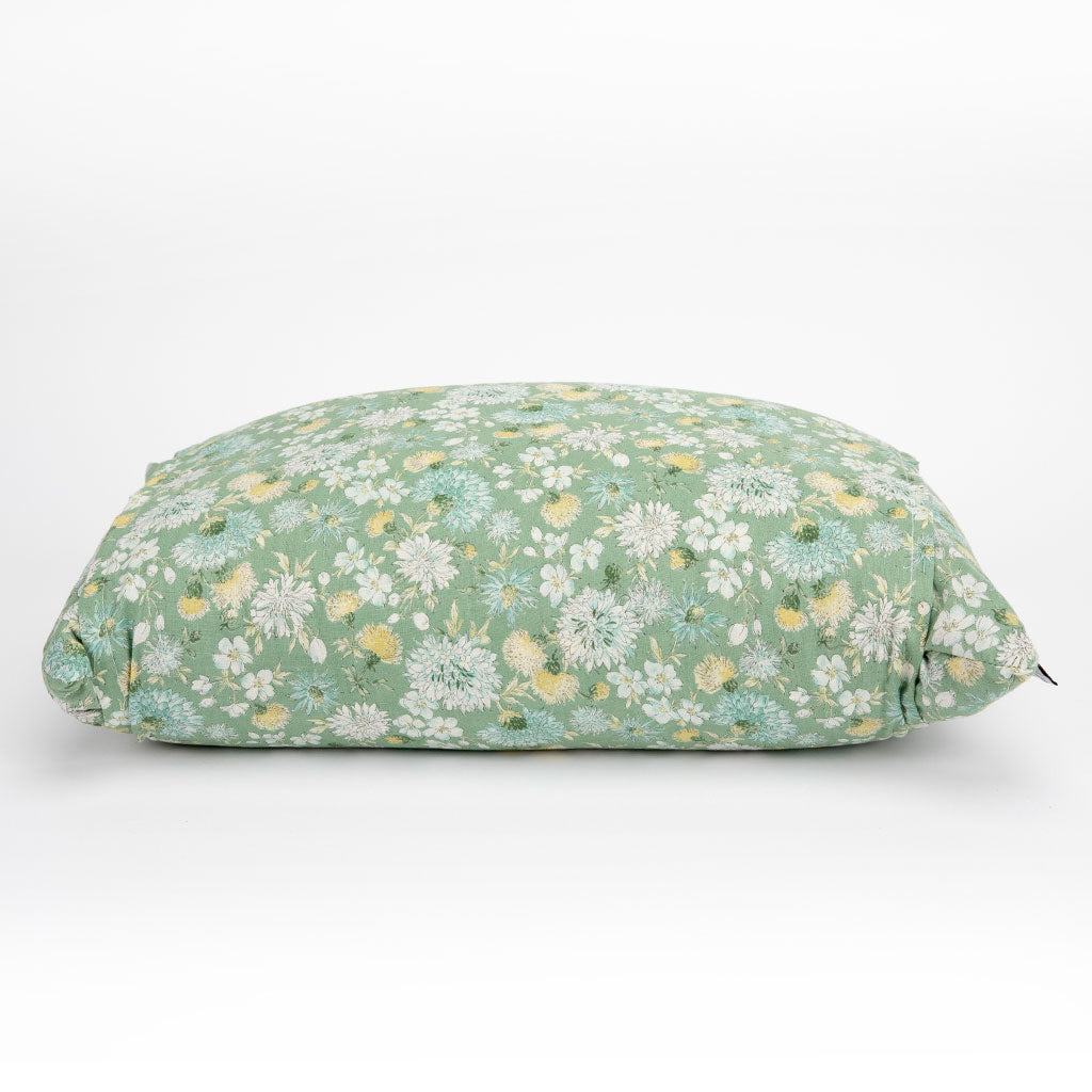 A rectangular buckwheat hull pillow with a sage green floral print, featuring white and yellow flowers, photographed on a seamless white background.