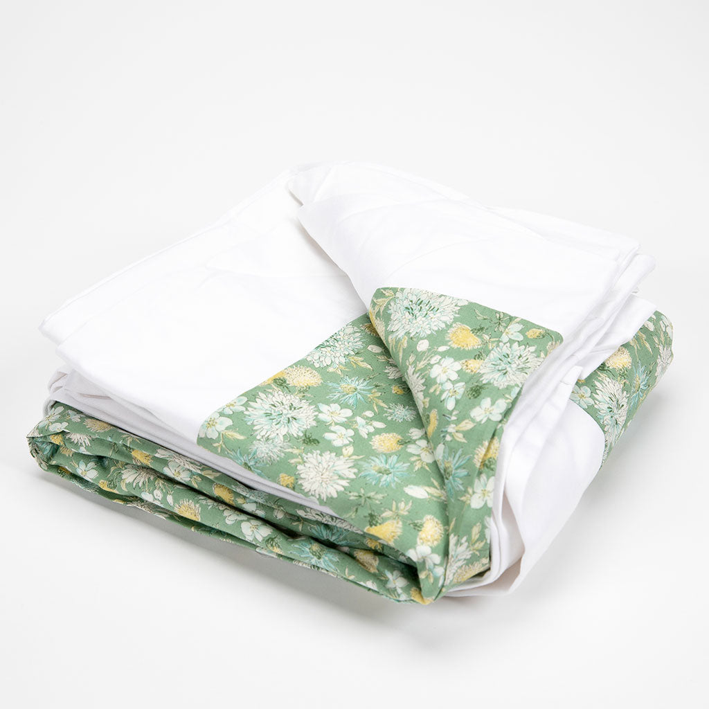 A folded bedding set, likely a duvet cover and pillowcases, featuring solid white fabric and a green floral patterned fabric, photographed on a clean white background.