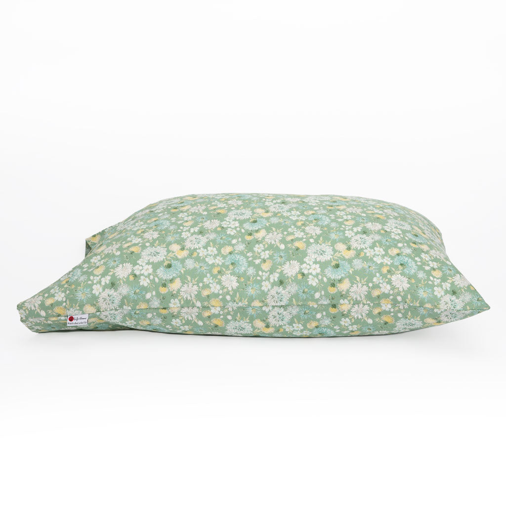 A rectangular pillowcase with a sage green floral pattern, featuring small white, yellow, and light blue flowers. A small white brand tag is visible on the lower left corner.