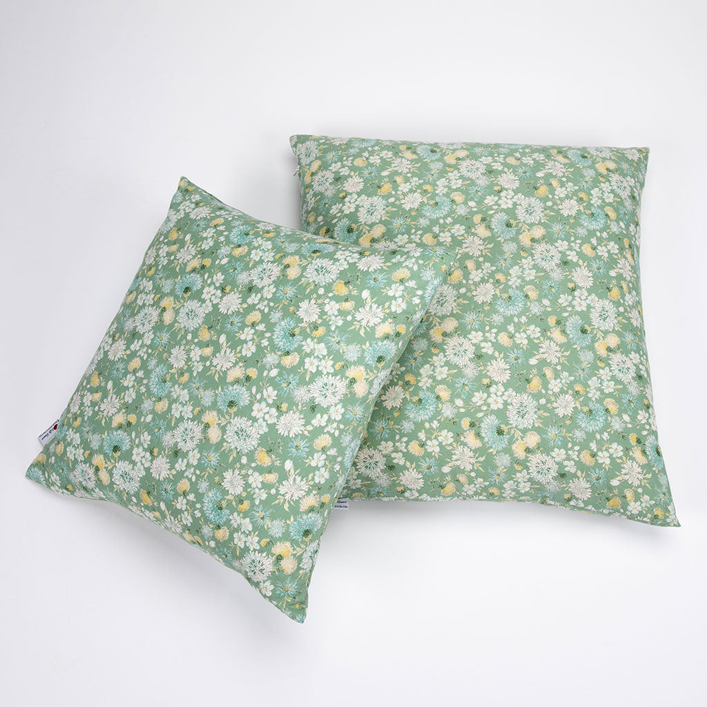 Two square throw pillows with a green floral print, featuring white and yellow flowers, arranged on a plain white background.