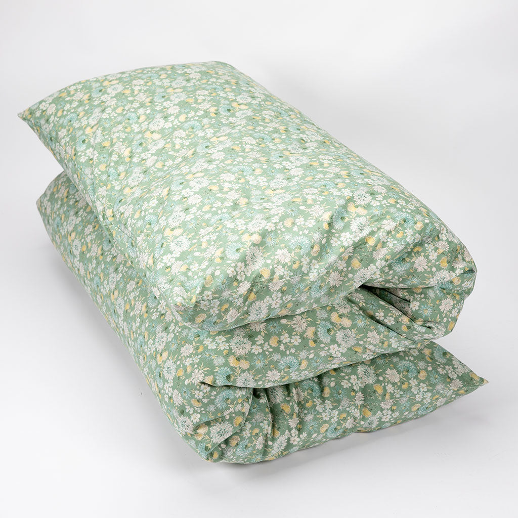 A folded quilt or comforter with a dense small floral print in sage green, white, and soft yellow, photographed on a clean light gray studio background.