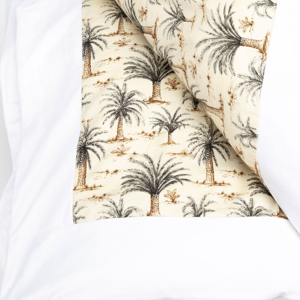 A folded kakefuton featuring a cream background with a repeating palm tree pattern in dark charcoal and tan. It is shown layered over a plain white fabric background.