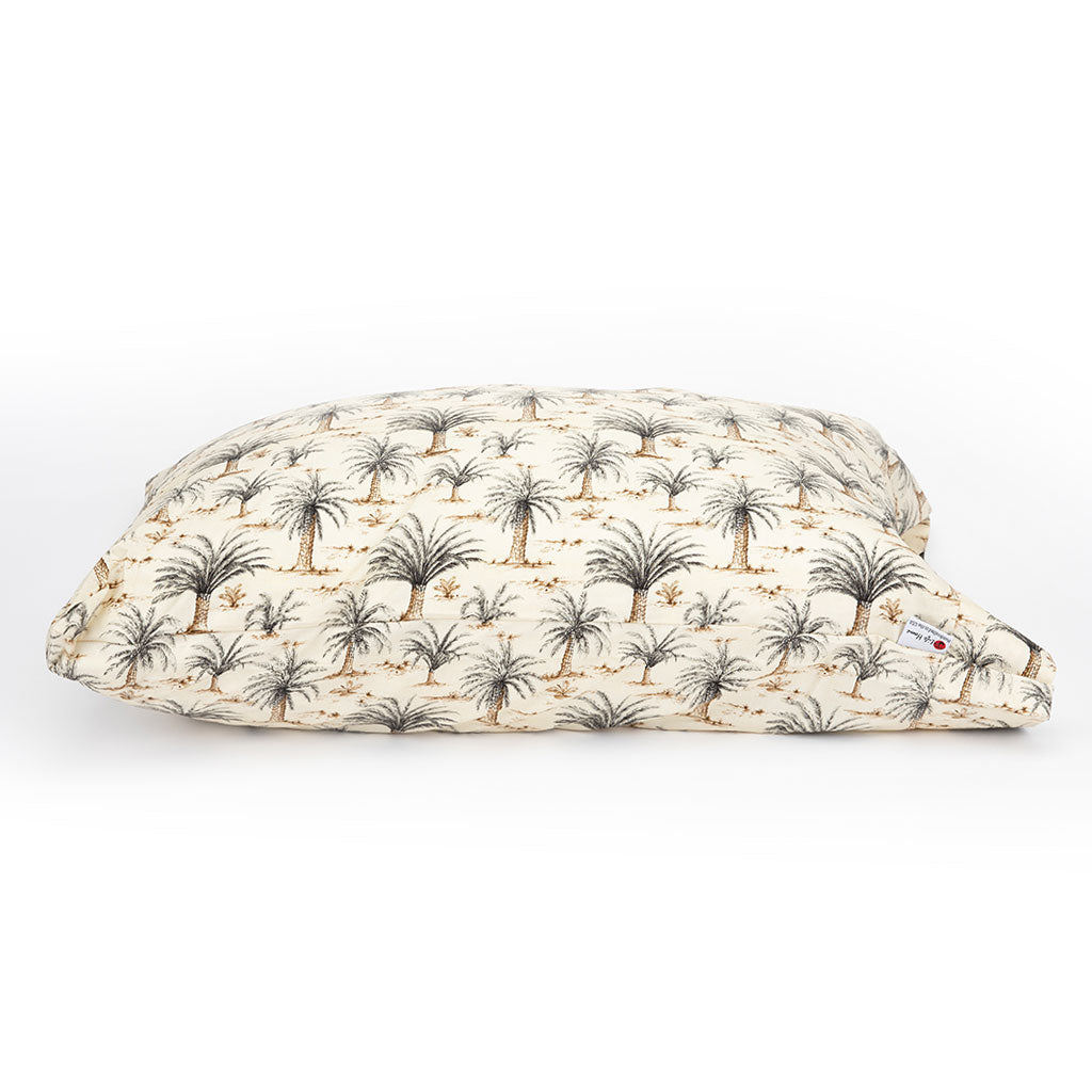 A rectangular cushion or pillow with a cream-colored fabric printed with a repeating pattern of palm trees and small cacti in dark gray and light brown, shown on a clean white background.