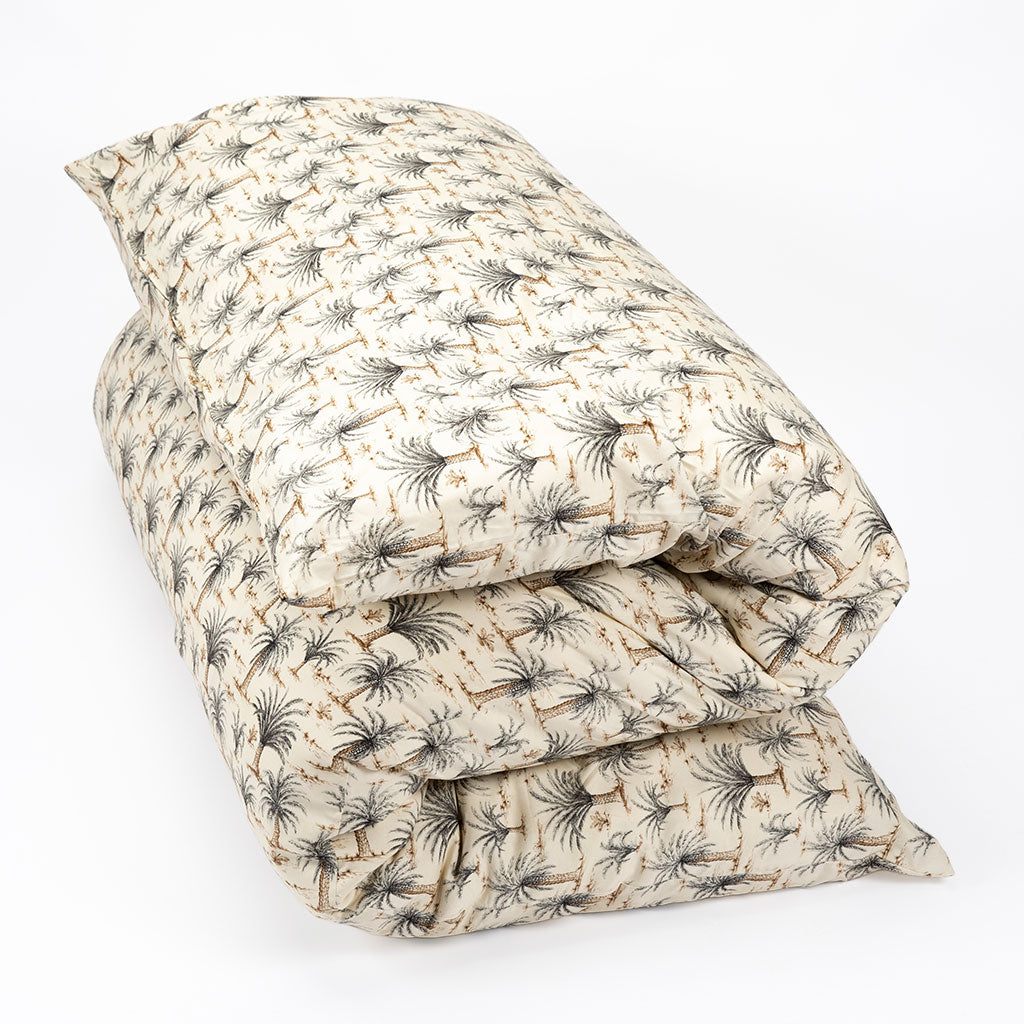 A folded shiki futon or shikibuton with a repeating palm tree print on a warm cream background, photographed on a clean white studio background.