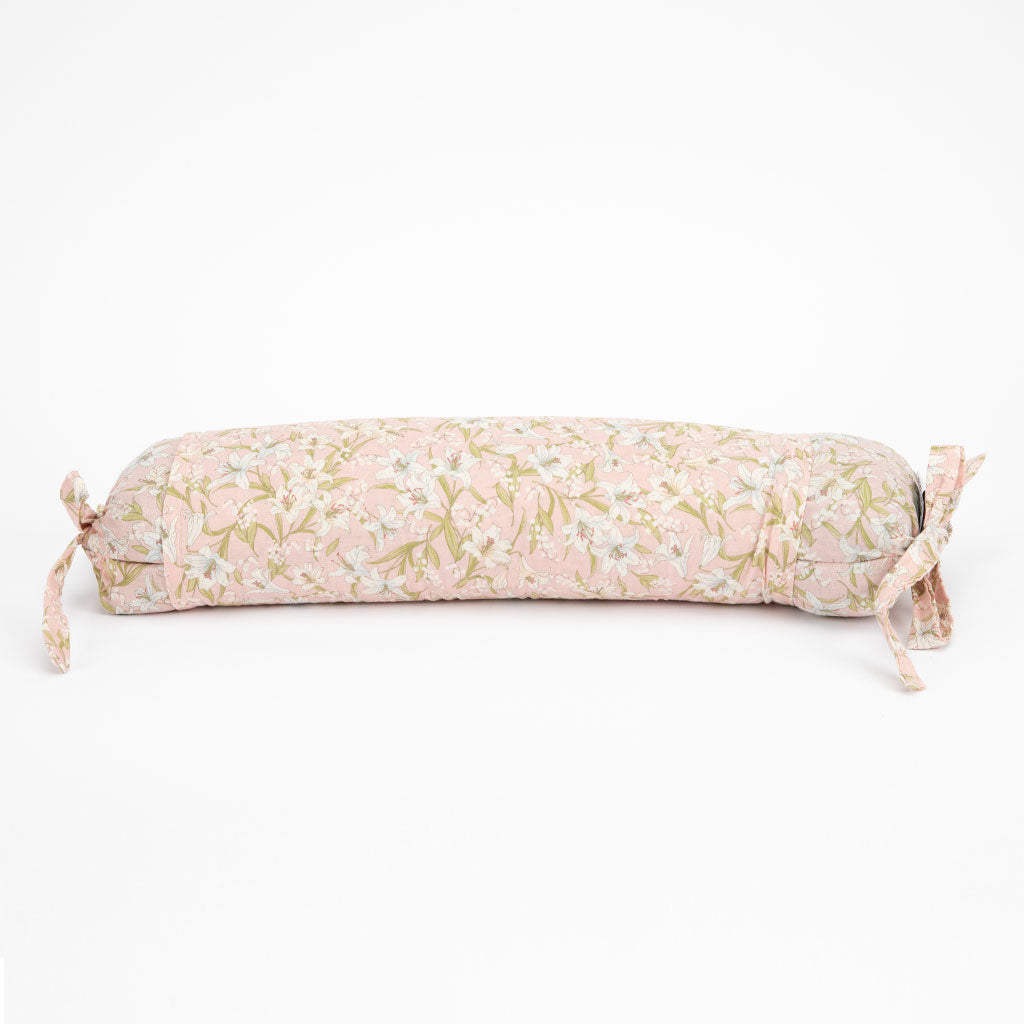 A long cylindrical buckwheat hull pillow with a light pink and white floral pattern and olive green leaves, featuring tie-on ends, shown on a plain white background.