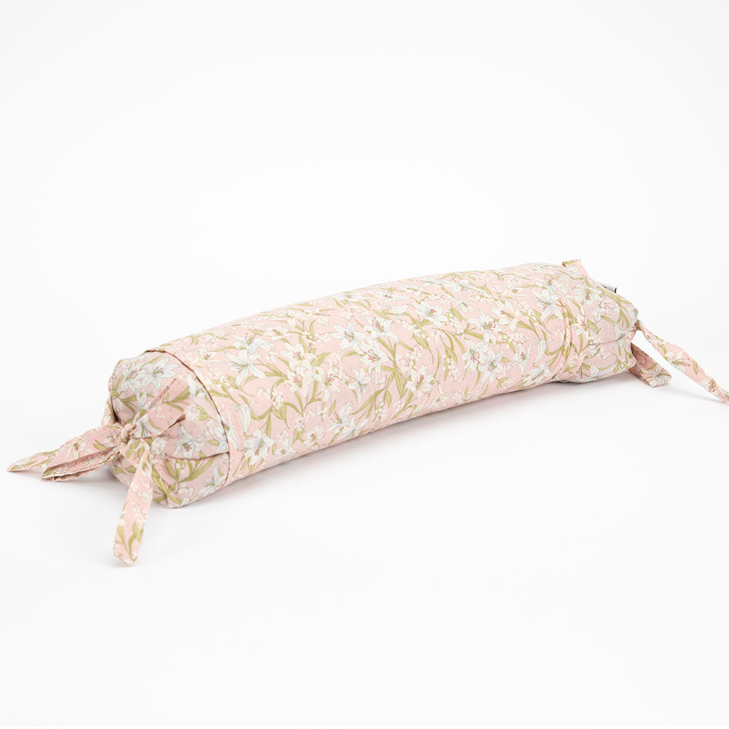 A cylindrical rectangular buckwheat hull pillow with a light pink and beige floral pattern, featuring tie-on straps at both ends, shown on a plain white background.