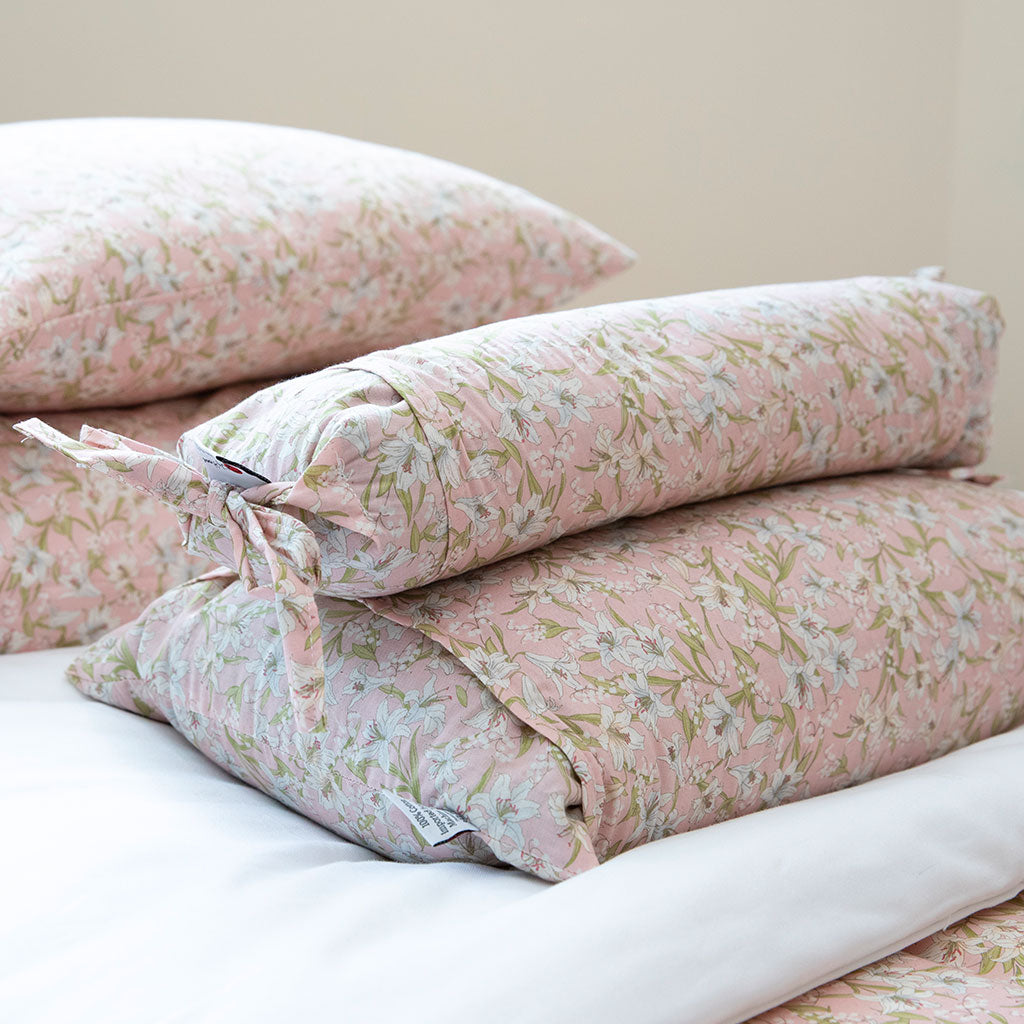 A stack of pink floral bedding, including a folded duvet cover and two matching pillowcases, displayed on a white sheet against a soft beige background.