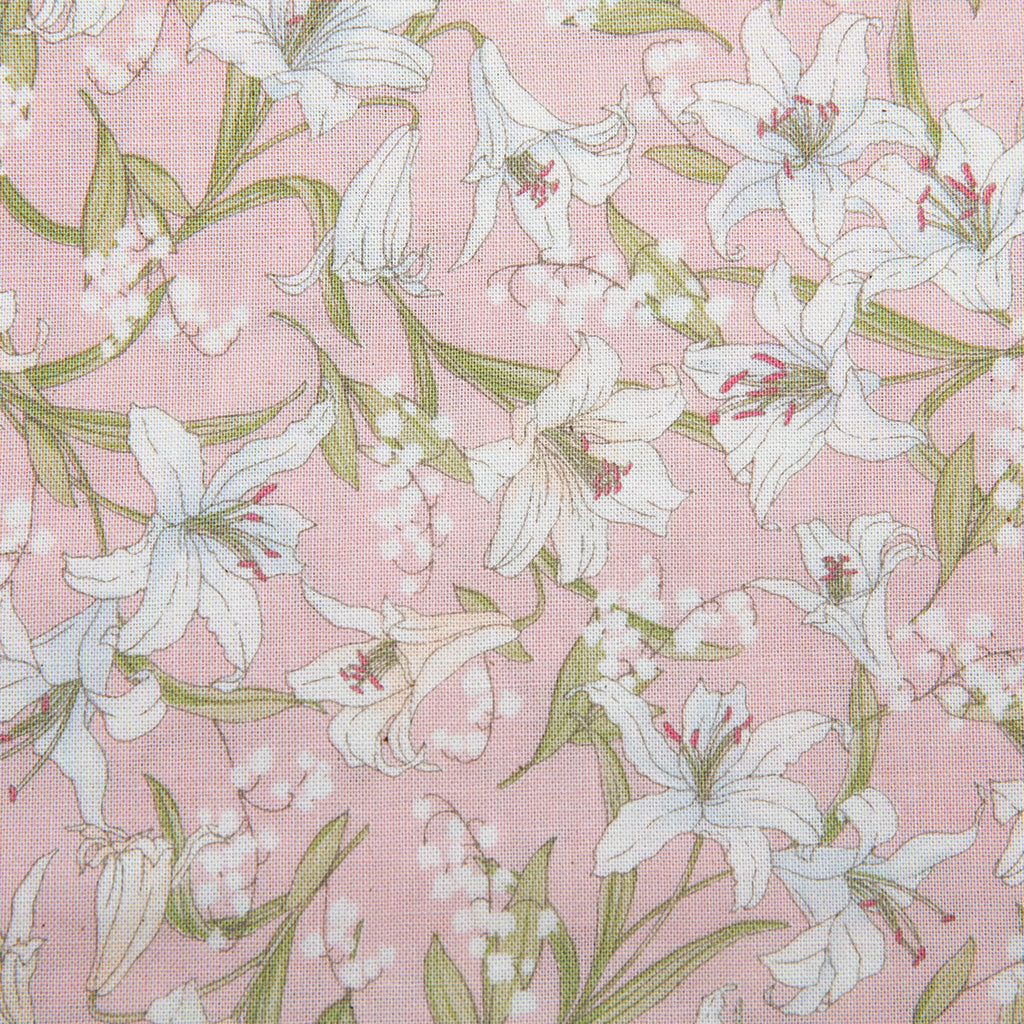 A close-up of a pink floral fabric featuring white lilies with green leaves and stems, accented by small white bell-shaped flowers.