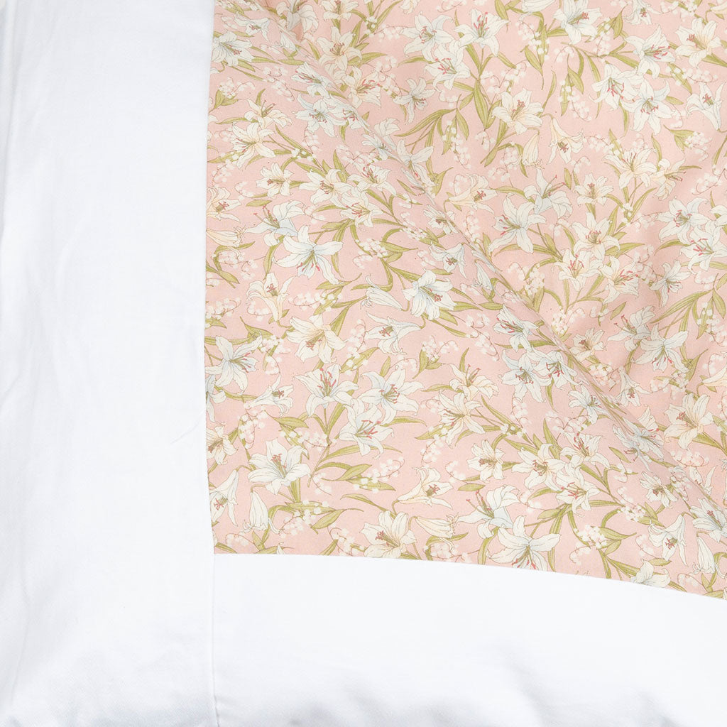 A close-up of a quilted bedding fabric panel featuring a light pink background with a white and pale green floral pattern, bordered by solid white fabric on the sides.