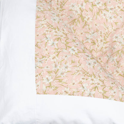 A close-up of a quilted bedding fabric panel featuring a light pink background with a white and pale green floral pattern, bordered by solid white fabric on the sides.