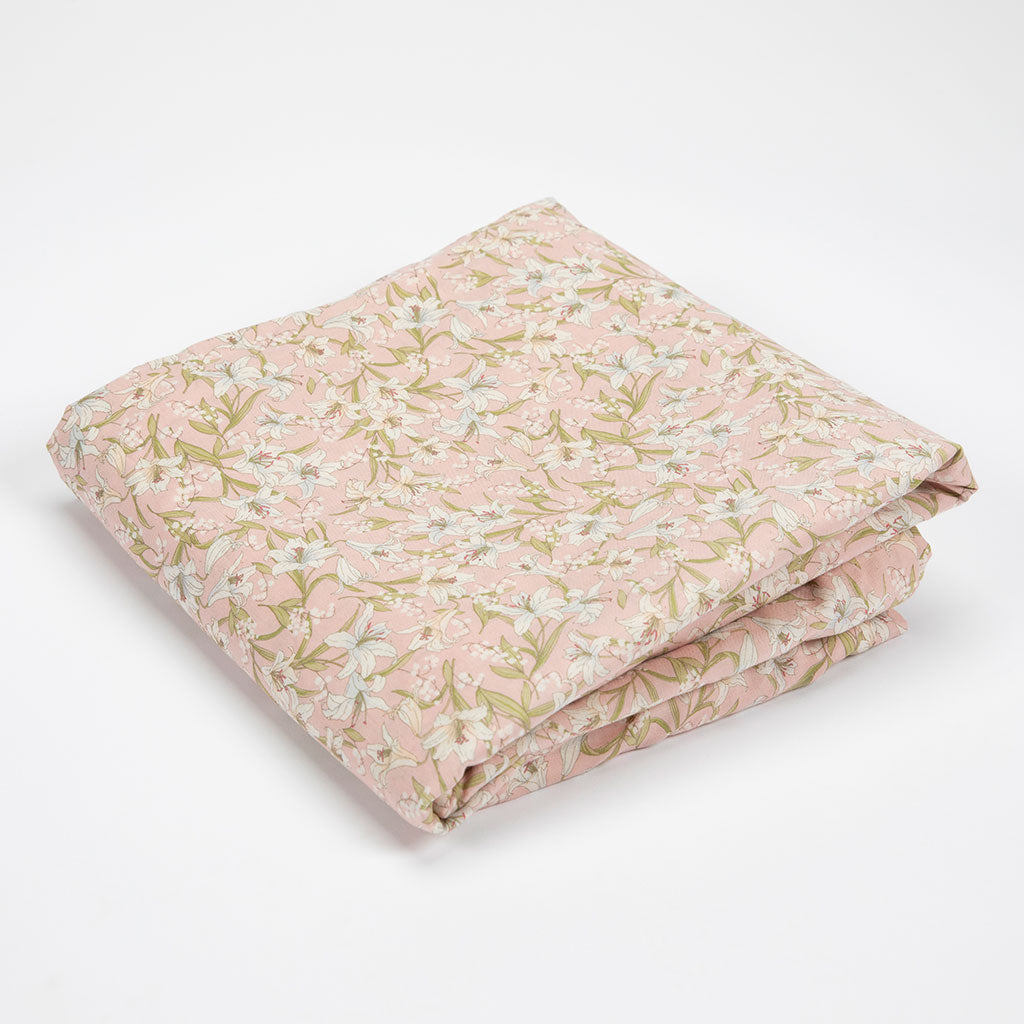 A folded piece of light pink fabric with a delicate floral and leaf pattern in soft green, beige, and white, displayed on a clean white background.