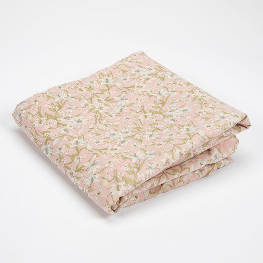 A folded piece of light pink fabric with a delicate floral and leaf pattern in soft green, beige, and white, displayed on a clean white background.
