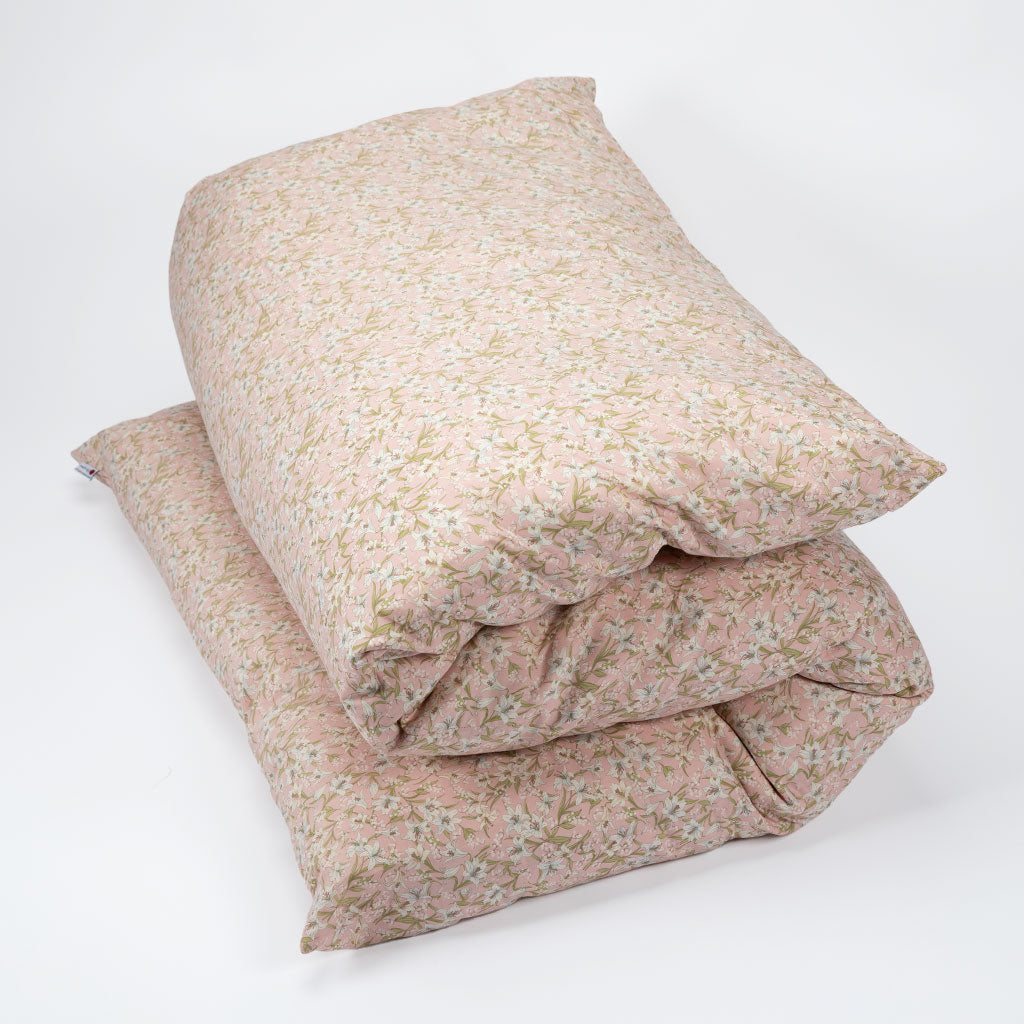 A stack of two folded bedding pieces, likely pillows or a folded duvet/comforter, covered in a light pink floral print with small green and beige blossoms, photographed on a clean white background.