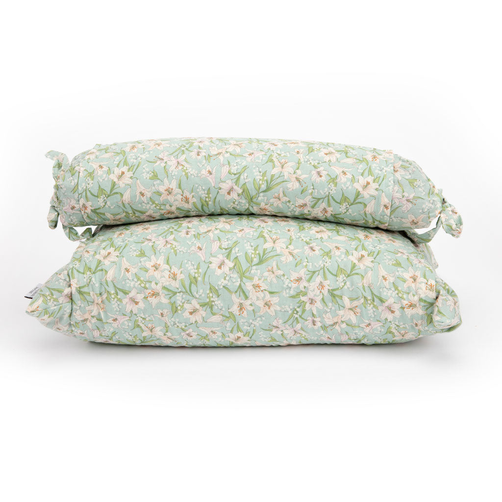 Two cylindrical buckwheat hull pillows stacked on top of each other, featuring a light mint green and white floral print with green leaves.