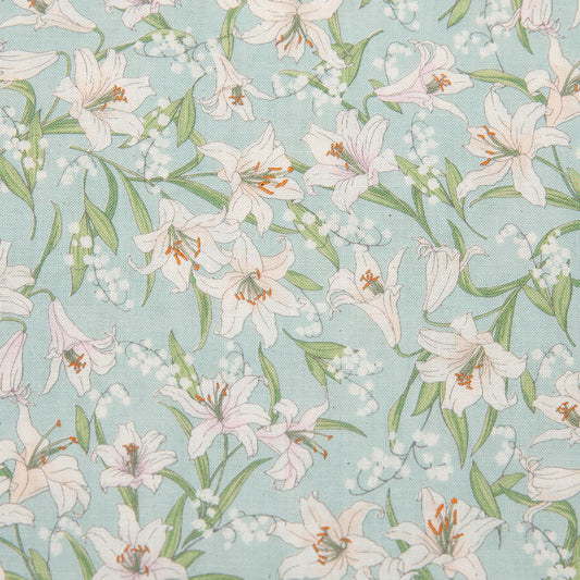 A close-up of a fabric pattern featuring white and pale pink lilies with green leaves and small white flowers on a light blue background.