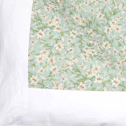 A close-up of a bedding featuring a light mint green background with a delicate white and pale pink lily floral pattern, bordered by a wide white band on the left.