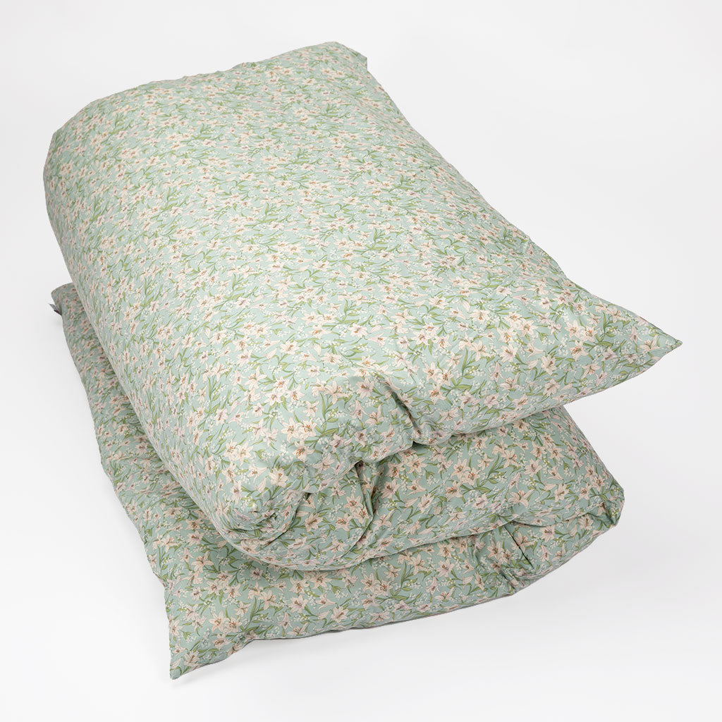 A folded shikifuton featuring a light sage green floral and leaf pattern with small pink and white blossoms, set against a plain white background.