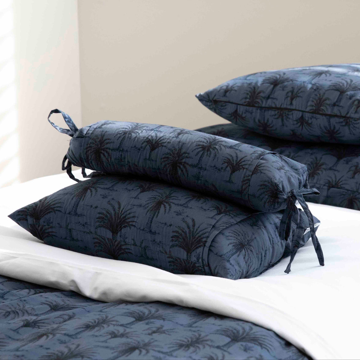 A navy blue quilted comforter set with a dark palm tree pattern, styled on a bed with white sheets and matching pillows.
